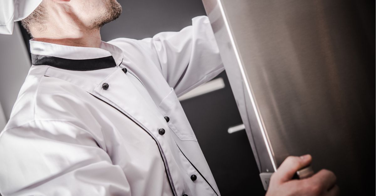 Cocinero revisando un equipo de refrigeración industrial en cocina profesional Cocinero revisando un equipo de refrigeración industrial en cocina profesional.